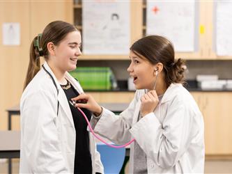 A student is using a stethoscope on another student