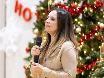 Woman speaking into mic in front of christmas tree