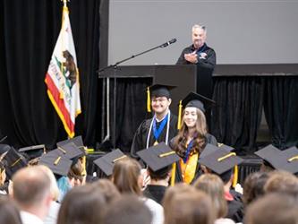 Students standing in audience for recognition, man standing at podium on stage