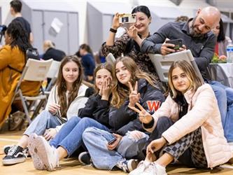 Students sitting on gym floor giving peace sign