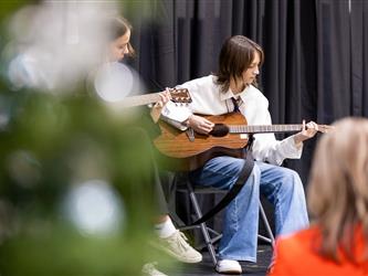 Teen playing guitar with christmas tree in foreground