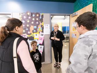 A teacher greets a parent and her kids at the door