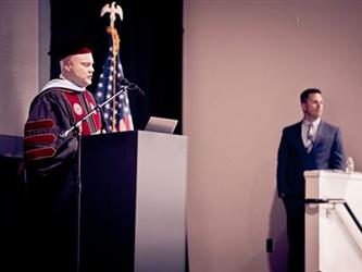Two men stand on stage awaiting graduates