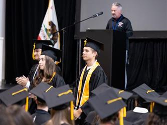 Students standing in audience for recognition, man standing at podium on stage