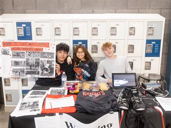 3 students are sitting at their wrestling display table